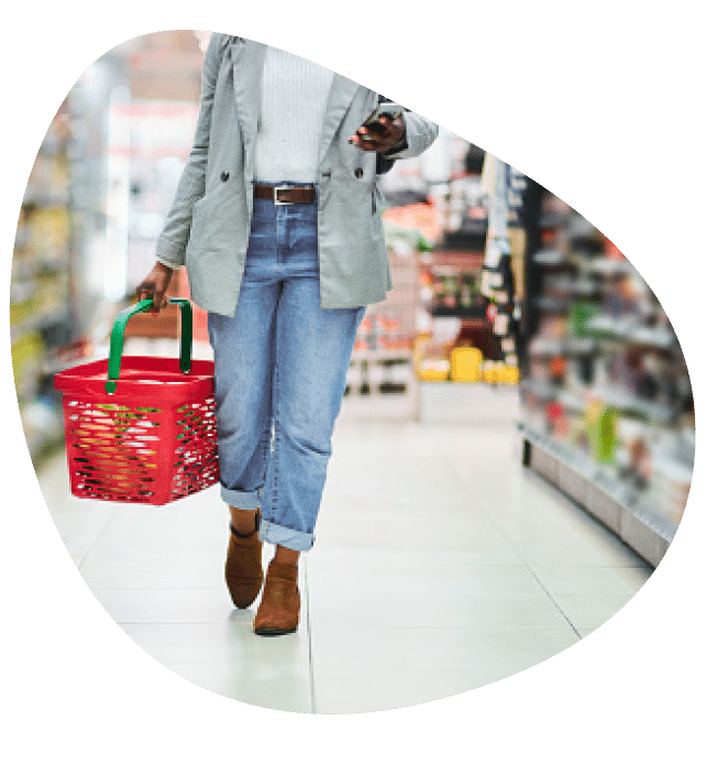 Bottom half of a person walking through supermarket aisle holding a red basket